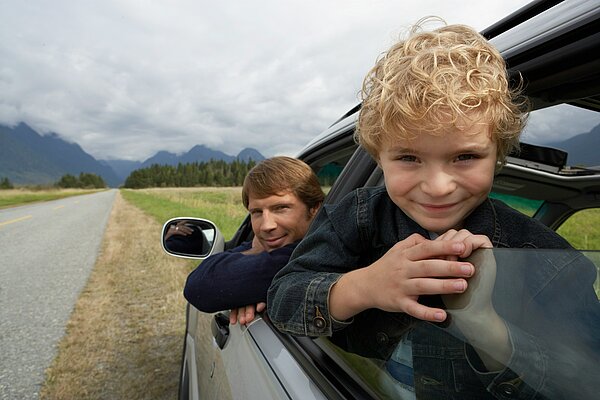 Das Bild zeigt einen Vater und seinen Sohn, die gemeinsam im Auto sitzen. Der Junge lehnt sich fröhlich aus dem Fenster, der Vater schaut entspannt zur Seite. Eine weite Landschaft mit Bergen und Wiesen zieht sich entlang der Landstraße – ein ruhiger, sicherer Moment.  Was auf den ersten Blick idyllisch wirkt, steht symbolisch für ein Thema, das viele Familien betrifft: Wir fahren unsere Kinder überall hin – aus Fürsorge, aus Zeitdruck, aus Angst. Doch echte Sicherheit entsteht nicht im Rücksitz. Sie entsteht durch Erfahrungen, durch Übung und durch das Vertrauen, dass Kinder selbst Lösungen finden können.  So wie der kleine Junge hier neugierig aus dem Fenster schaut, brauchen Kinder Räume, in denen sie wachsen dürfen. Räume, in denen sie selbst lernen, wie man sicher über die Straße geht, worauf es im Verkehr ankommt und wie man mit einem mulmigen Bauchgefühl umgeht.  👉 Denn: Mitfahren schützt – aber nur kurzfristig. Selbstständigkeit schützt fürs Leben.