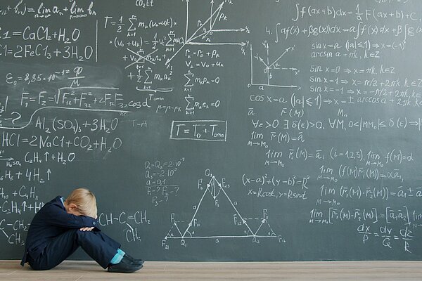 Ein Kind sitzt mit gesenktem Kopf vor einer Tafel voller mathematischer Formeln und wirkt überfordert.