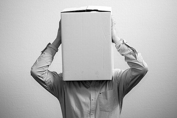 Mitarbeiter mit einem Karton über dem Kopf symbolisiert Unsicherheit und Orientierungslosigkeit während einer Unternehmenskrise.