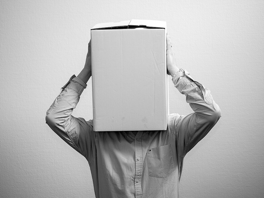 Krisenzeiten im Unternehmen – Unsicherheit erfolgreich bewältigen Mitarbeiter mit einem Karton über dem Kopf symbolisiert Unsicherheit und Orientierungslosigkeit während einer Unternehmenskrise.